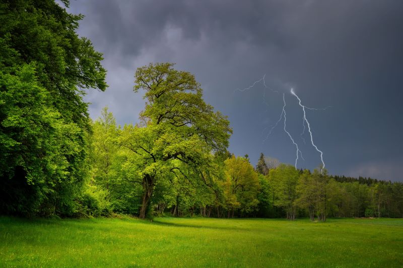 Promenljivo oblačno i nestabilno vreme iznad prirodnog pejzaža, tamni olujni oblaci, jaka kiša i munje koje paraju nebo, vetrovita atmosfera pred nevreme.