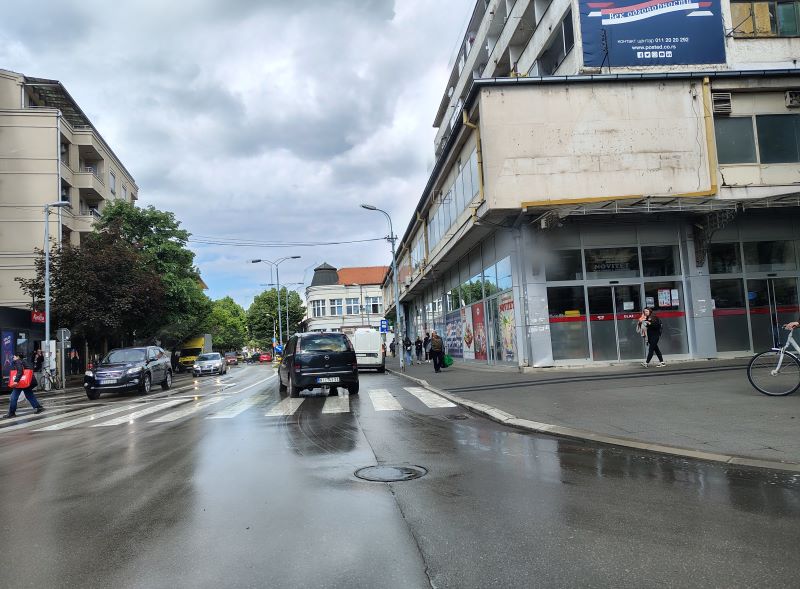 Kišna ulica u Požarevcu sa mokrim kolovozom, automobili u pokretu, pešaci i refleksija svetla na asfaltu